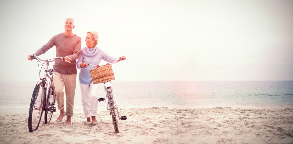 Happy retired couple with bikes on the beach